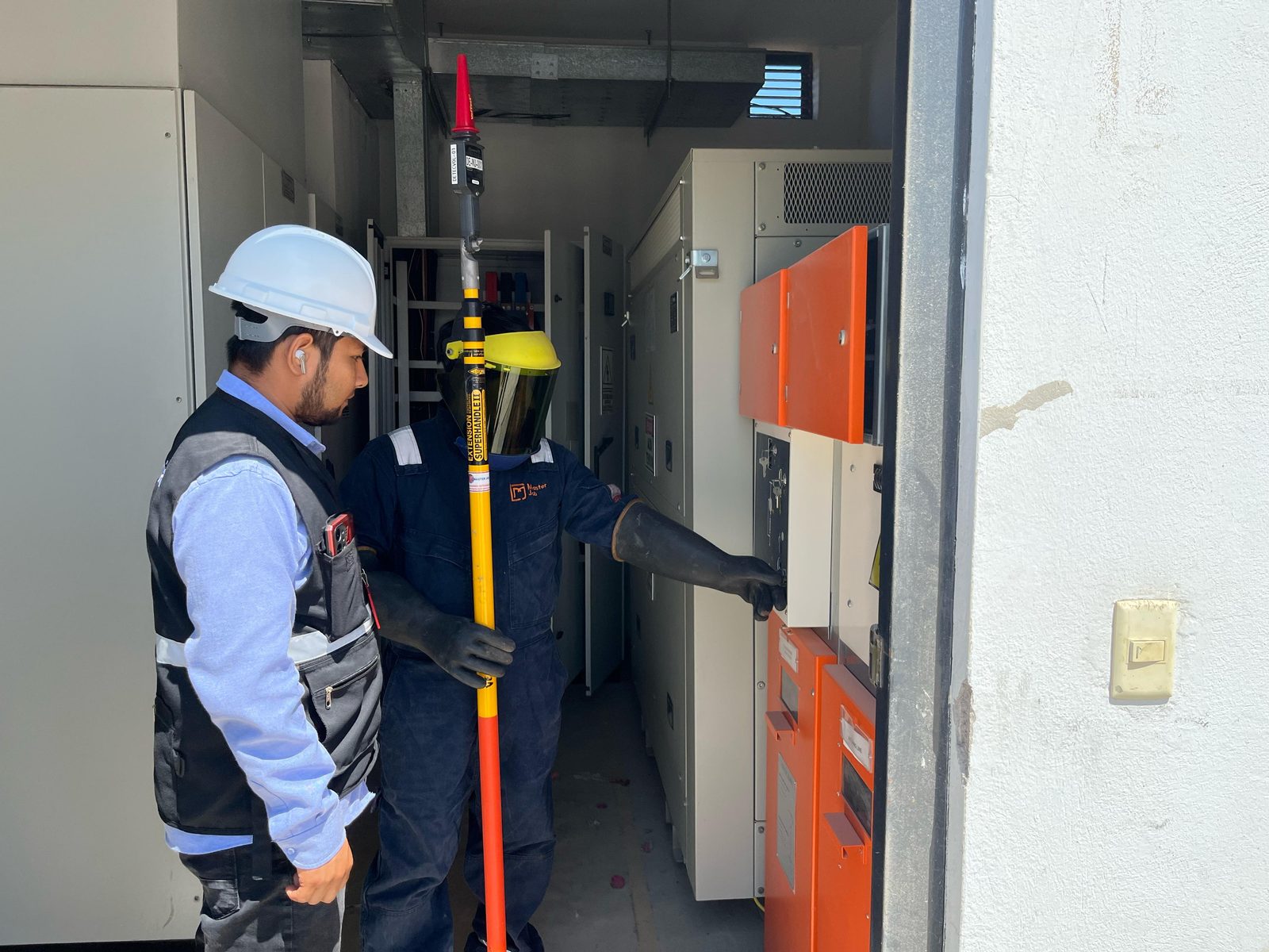 Técnico de Master Job con careta de protección y guantes dieléctricos maniobrando una celda de media tensión, con un supervisor observando la operación.